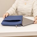 Donkerblauwe laptoptas op een tafel. Een laptop wordt eruit gehaald.