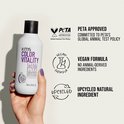 Hand met paarse nagellak die een KMS Color Vitality Blonde Conditioner fles vasthoudt, met PETA- en vegan-logo's.