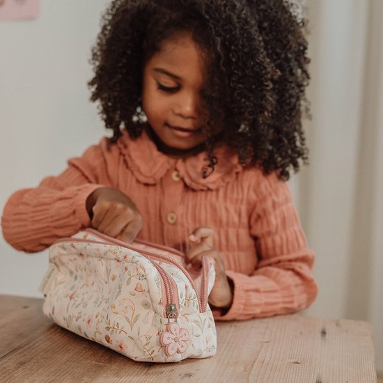 Meisje met krullend haar opent een etui met een bloemenprint in zachte kleuren.