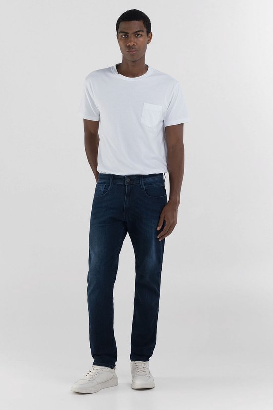 Man met donkere spijkerbroek en witte t-shirt, handen in zakken.