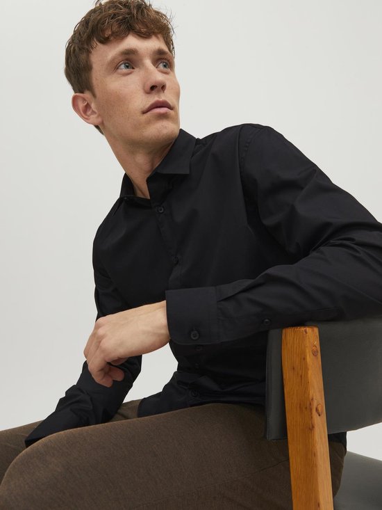 Man in zwart, lang-mouwig button-down overhemd, zittend op een stoel.