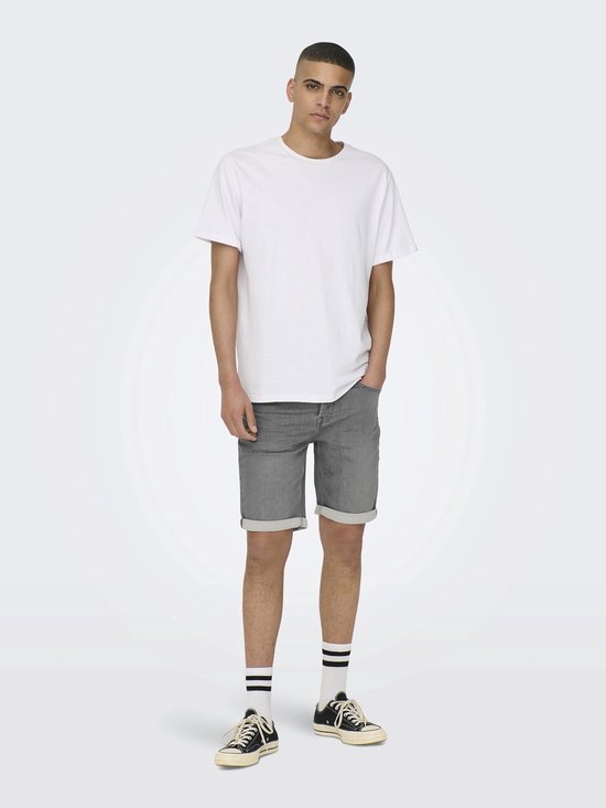 Man met witte T-shirt en grijze denim shorts met omgeslagen broekspijpen.