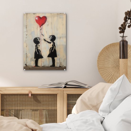 Twee silhouetten van meisjes op een muur met verfspatten, één meisje laat een rood hartvormige ballon los.