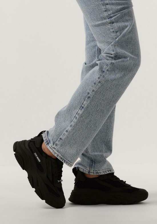 Voeten in blauwe jeans en zwarte Steve Madden sneakers met dikke zolen.