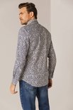 Model draagt een wit overhemd met een all-over print in blauw, rood en oranje. Het shirt heeft lange mouwen en een button-down kraag.