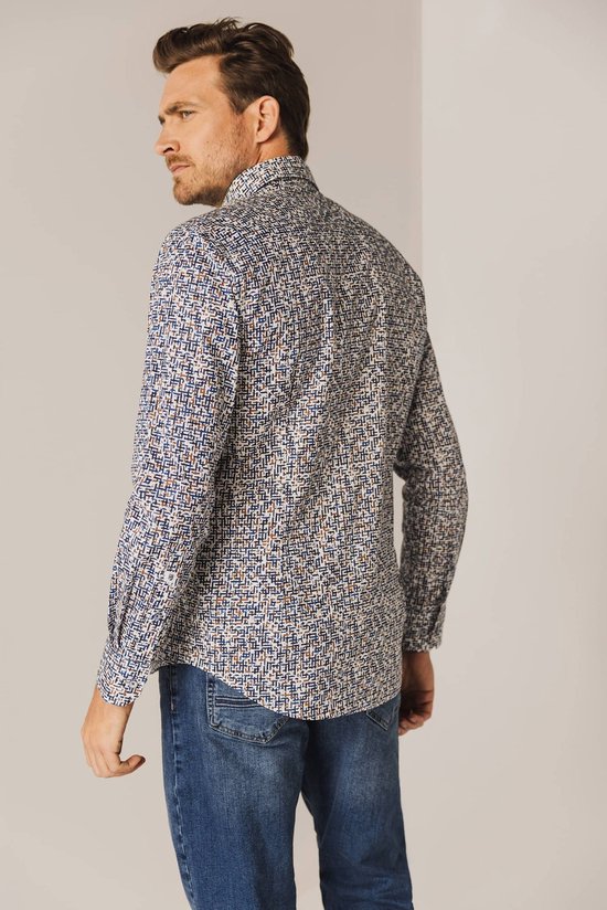 Model draagt een wit overhemd met een all-over print in blauw, rood en oranje. Het shirt heeft lange mouwen en een button-down kraag.