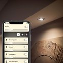 Een smartphone met de Hue app bedient een inbouwspot in een plafond.