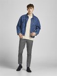 Model in grijze broek met visgraatpatroon, gestreepte top en spijkerjack.
