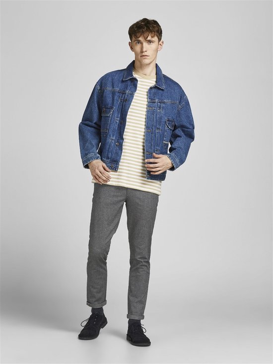 Model in grijze broek met visgraatpatroon, gestreepte top en spijkerjack.