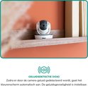 Witte babyfoon camera op een plank in een kamer met oranje muur. 'Geluidsdetectie (VOX)' icoon.