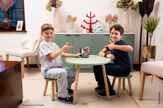 Twee jongens zitten aan een tafel en wijzen naar een groene Skip-Bo draagtas.
