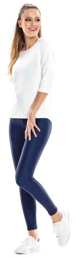 Vrouw in witte driekwart top en donkerblauwe glanzende legging, witte sneakers, zijwaarts.