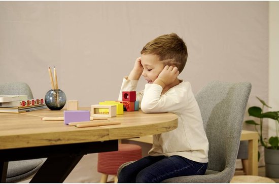 Een jongetje met bruine haren, zittend aan een tafel, kijkt geconcentreerd naar zijn houten blokken.
