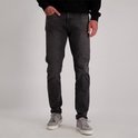 Man met donkere spijkerbroek en grijze sneakers, hand in broekzak.