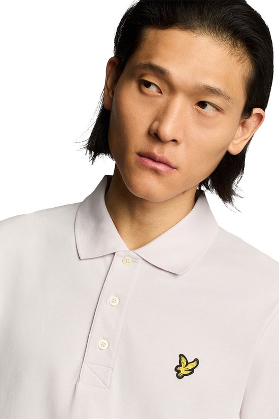 Close-up van man met lichtroze poloshirt, gele vogel-logo zichtbaar.