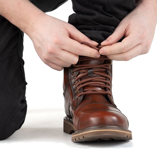 Handen strikken de veters van een bruine leren motorlaars, gedragen met een zwarte broek.