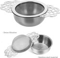 Zilverkleurige theezeef met gaasfilter en dubbele vleugel handvatten, naast een zilverkleurig lekbakje. "Dense filtration" en "Stainless steel material" tekst.
