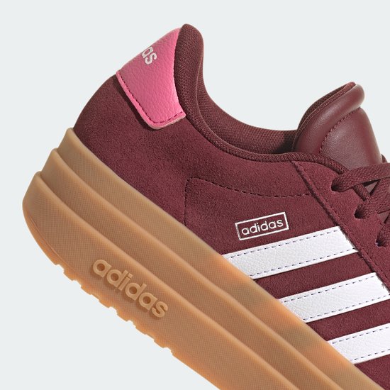 Close-up van een bordeauxrode Adidas sneaker met roze hielkap, dikke gum-zool en witte strepen.