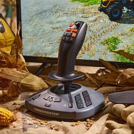 Zwarte Thrustmaster joystick met oranje knoppen op een grijze basis, omringd door herfstbladeren en maïskolven.