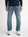 Man in een lichtblauwe loose fit jeans en een marineblauwe trui, met witte sneakers.