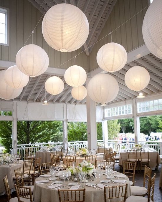 Royale eetzaal met hangende witte papieren lampionnen en gedekte tafels.