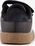 Achterkant van zwarte sneaker met witte strepen, bruine zool en klittenband.