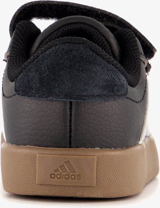 Achterkant van zwarte sneaker met witte strepen, bruine zool en klittenband.