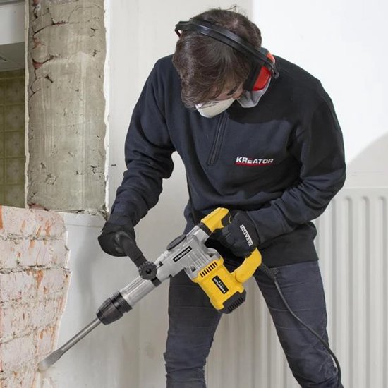 Man met veiligheidsuitrusting die met een gele en grijze breekhamer in een bakstenen muur hakt.