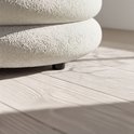 Detail van de crèmekleurige teddy stof van een ronde poef, met zwarte pootjes.