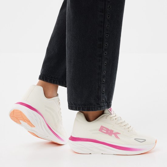 Dames die crème-kleurige sneakers met roze BK-logo en roze/oranje accenten dragen.