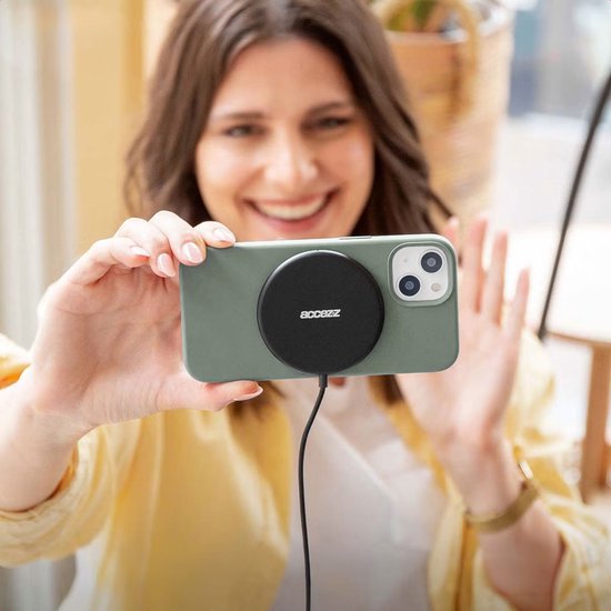 Vrolijke vrouw houdt een groene iPhone met MagSafe oplader vast.