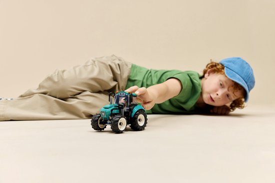 Jongen met blauwe pet ligt op de grond en speelt met een felgroene tractor.