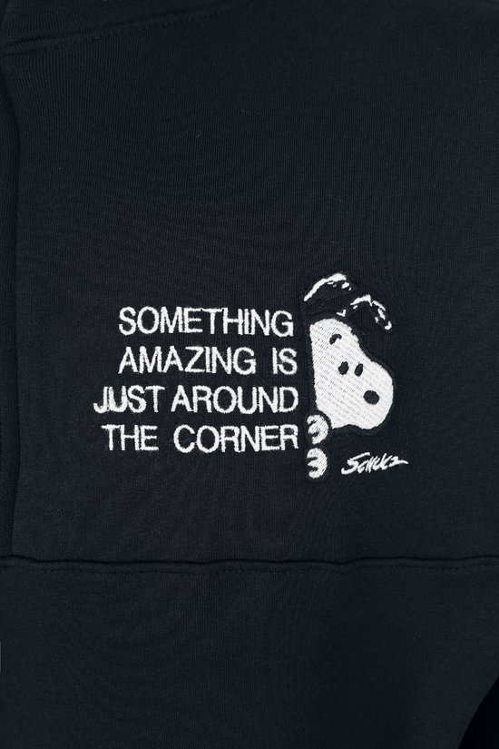 Detailopname van de witte borstprint op een zwarte trui met Snoopy en de tekst "SOMETHING AMAZING IS JUST AROUND THE CORNER".