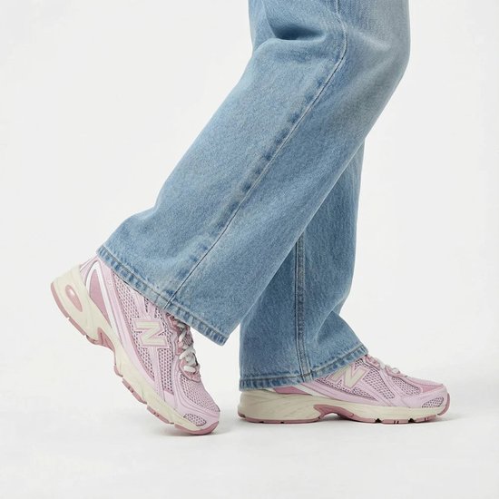 Lichtroze New Balance sneakers met beige zool, gedragen met een spijkerbroek.