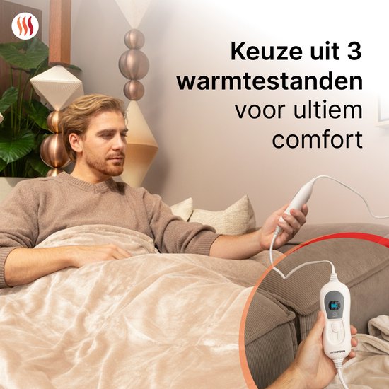 Man zit op bank met beige elektrische deken, houdt bediening vast. Tekst: 'Keuze uit 3 warmtestanden voor ultiem comfort'.