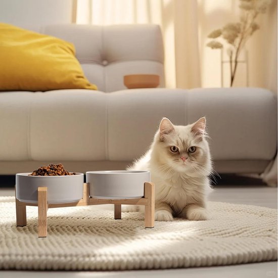 Grijze keramische dubbele voerbak op een houten standaard met een kat die ernaast ligt.