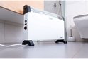 Witte convector met zwarte accenten en pootjes, staand op een grijze tegelvloer in een badkamer.