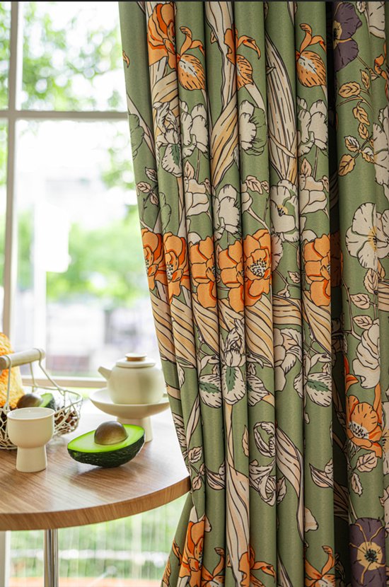 Groen gordijn met bloemenprint, gedrapeerd, met zicht op een tafel met avocado en kopjes.