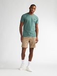 Man van voren gezien in een beige chino short met een groene t-shirt, witte sokken en sneakers.