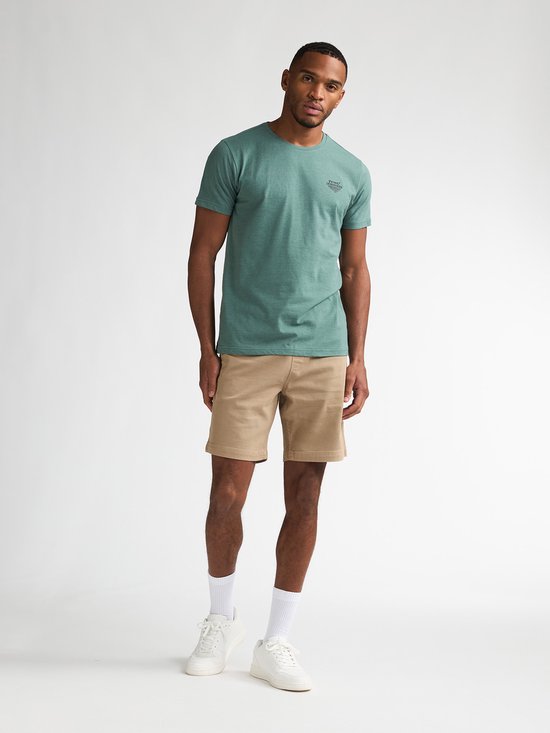 Man van voren gezien in een beige chino short met een groene t-shirt, witte sokken en sneakers.
