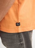 Detail van een oranje t-shirt met een zwart label met "PETROL INDUSTRIES SINCE 1993".