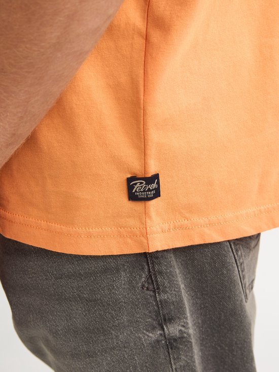 Detail van een oranje t-shirt met een zwart label met "PETROL INDUSTRIES SINCE 1993".