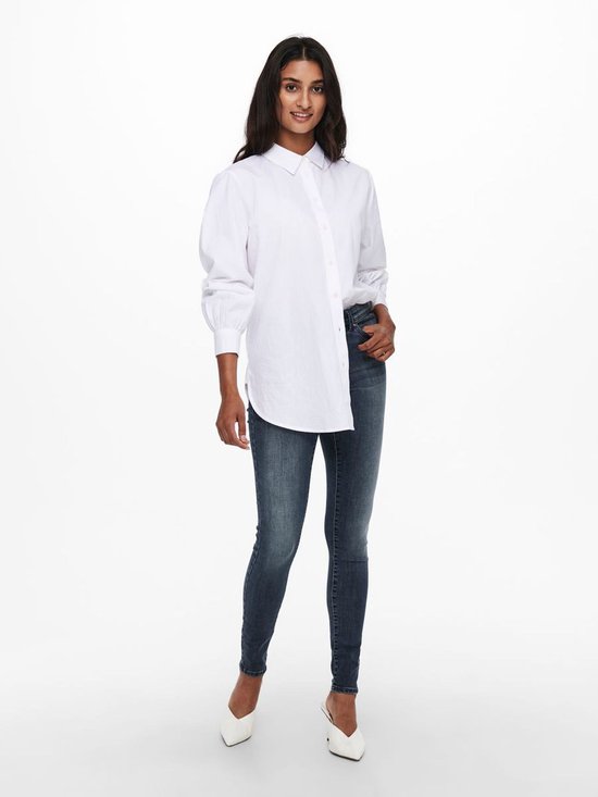 Model in een donkerblauwe skinny jeans met een witte oversized blouse.