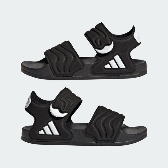 Twee zwarte Adidas Adilette kindersandalen met golvend patroon en drievoudig wit logo.