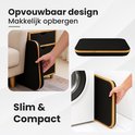 Opvouwbare zwarte wasmand, plat opgevouwen naast een kast en naast een wasmachine.