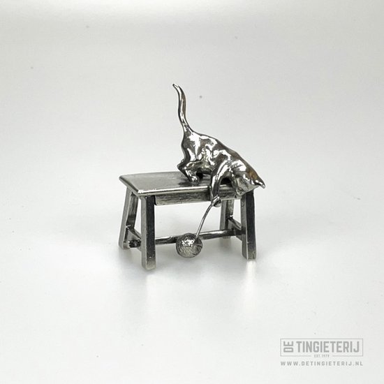 Une figurine en métal argenté brillant d'un chat joueur sur un petit tabouret avec une boule.
