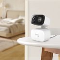 Witte Tapo beveiligingscamera op een tafel in een slaapkamer. Zwart camerahuis met lens.