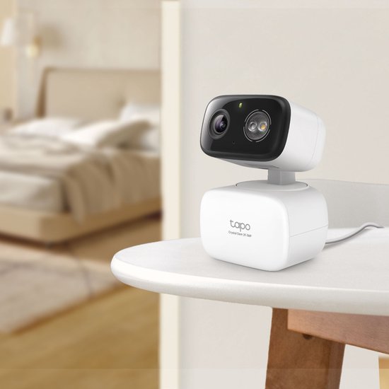 Witte Tapo beveiligingscamera op een tafel in een slaapkamer. Zwart camerahuis met lens.