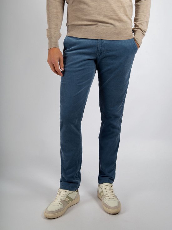 Man in beige trui en blauwe corduroy chino broek, staand.