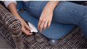 Vrouw met spijkerbroek die een mobiele powerbank aansluit op een blauw, verwarmd kussen in een rieten stoel.